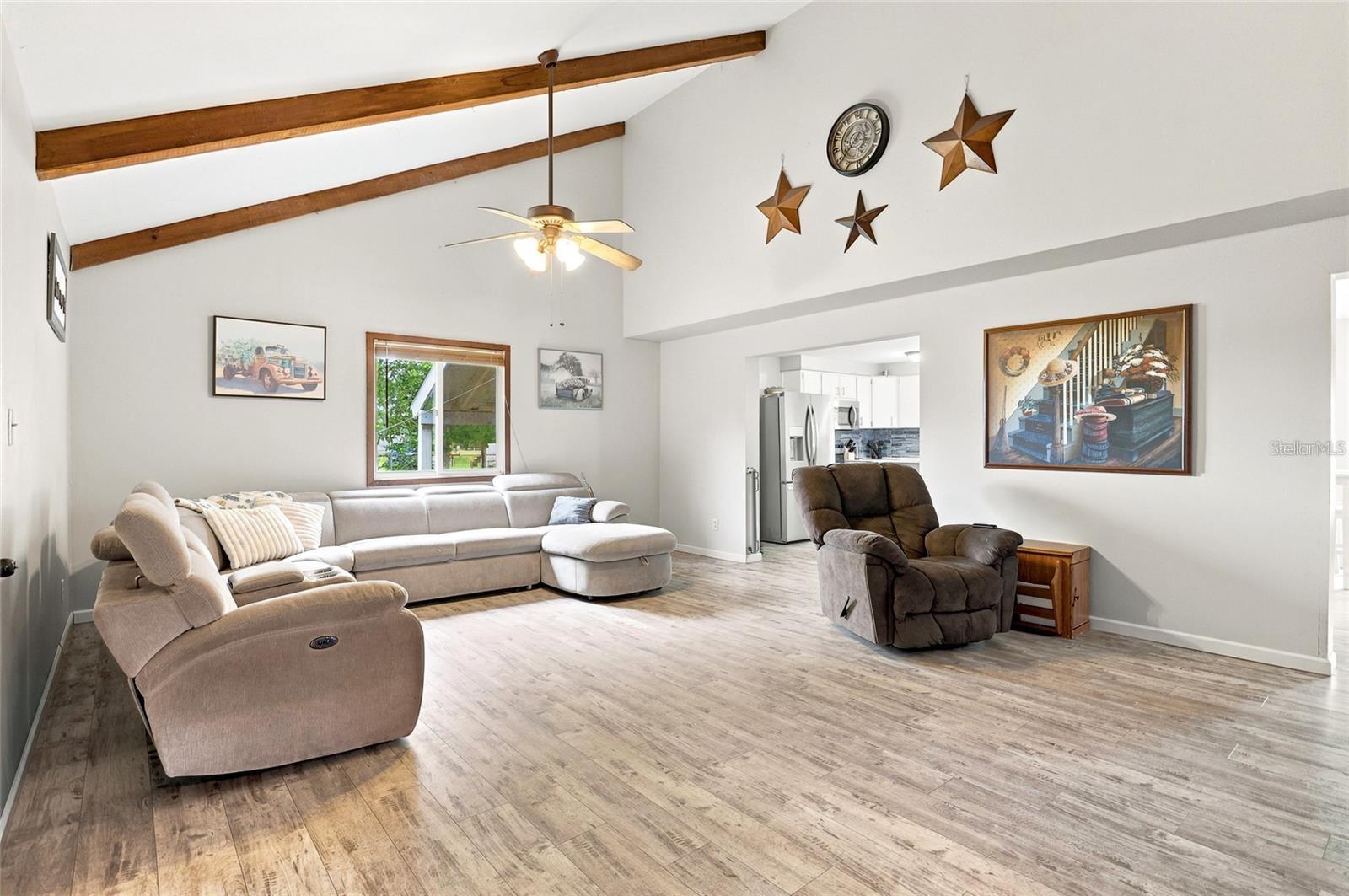 Living room with vaulted wood-beam ceiling, sectional sofa, recliner, and view into the kitchen.