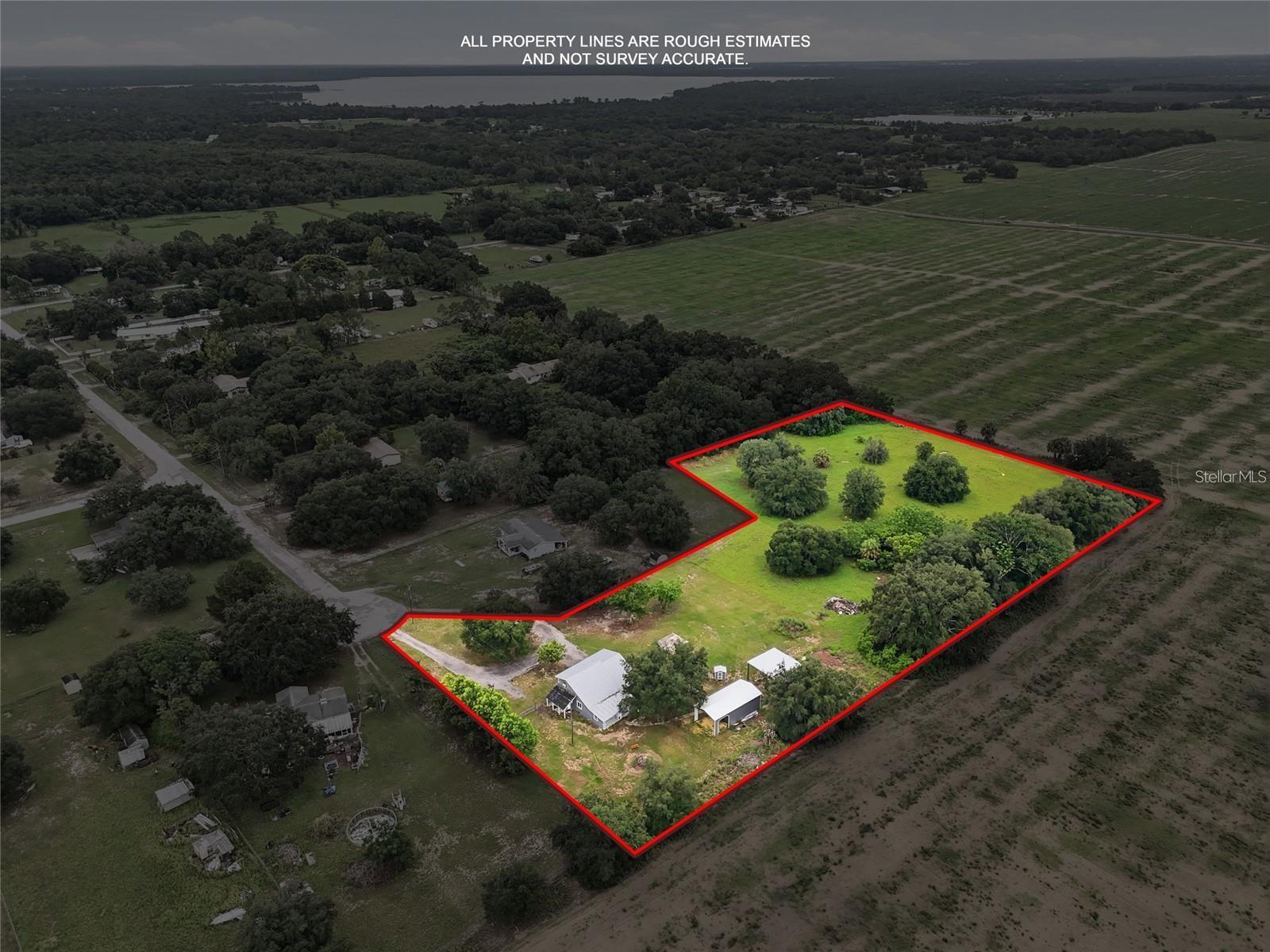Aerial view of a tree-dotted property outlined in red, with a house and covered structures.