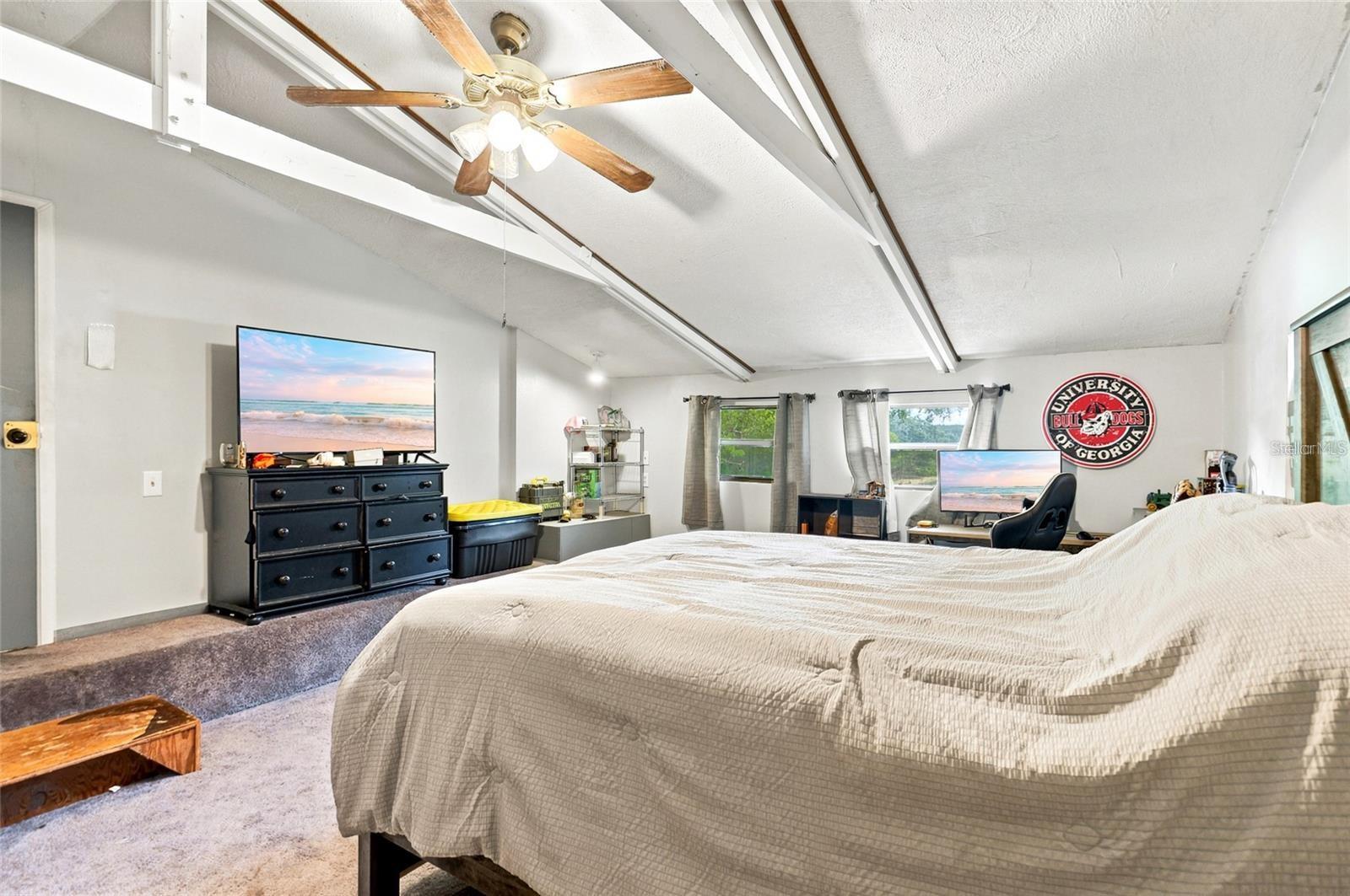 Furnished bedroom with a vaulted ceiling, ceiling fan, large bed, and University of Georgia wall sign.