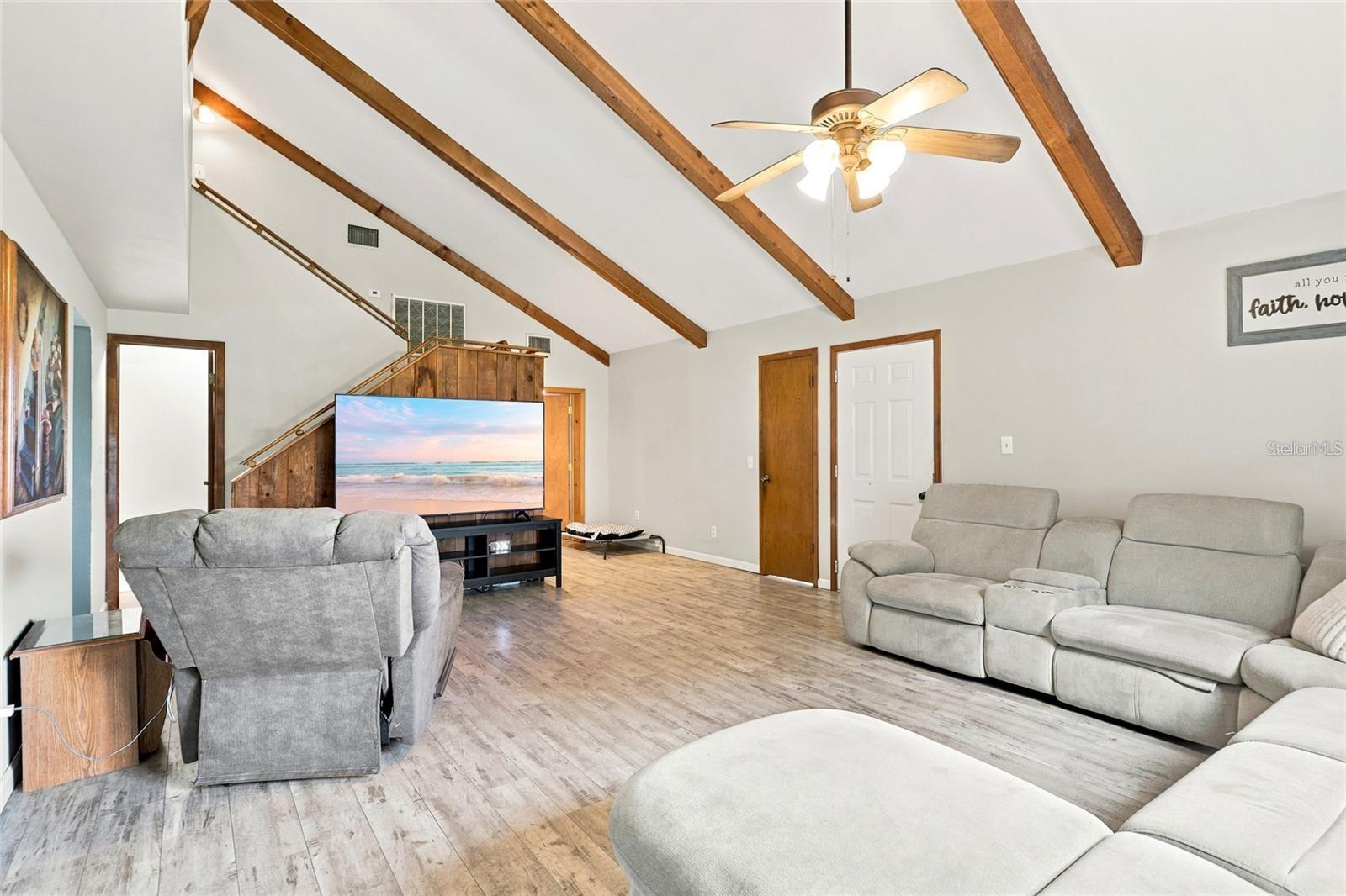 Living room with vaulted exposed-beam ceiling, gray sectional sofas, and staircase behind the television.