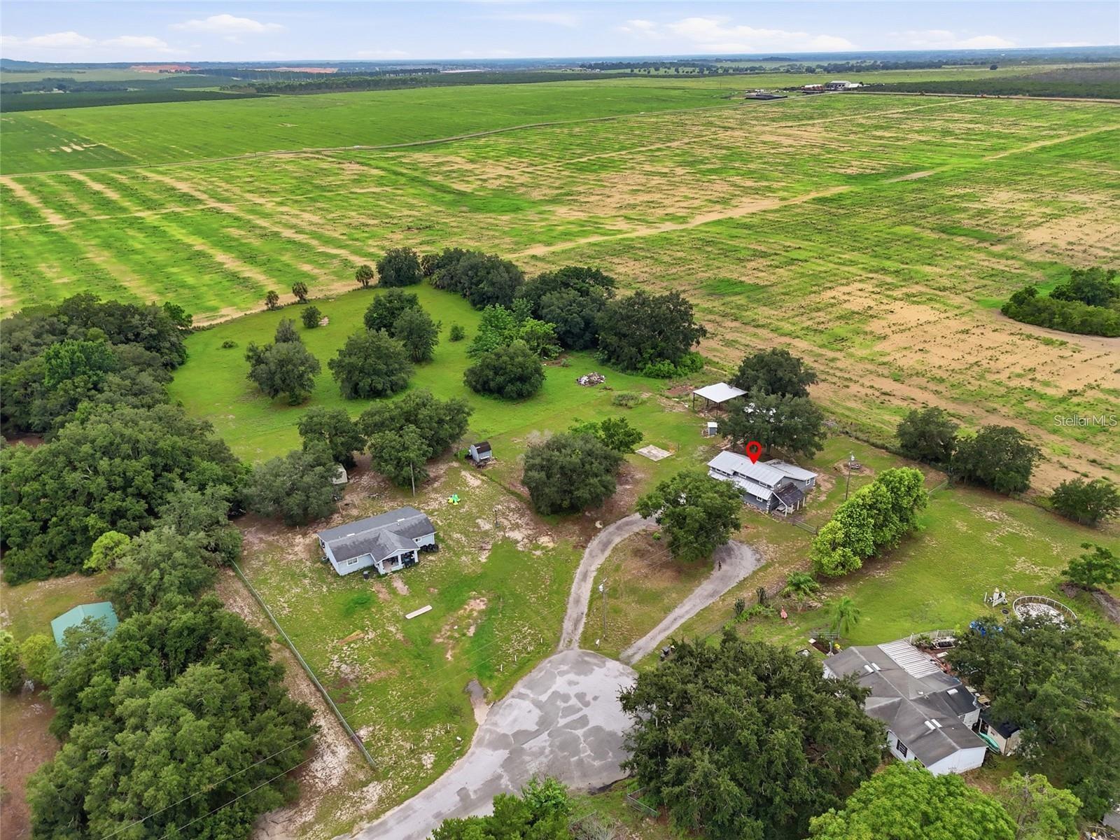 Aerial view of a rural home amid trees, with broad fields stretching across the surrounding landscape.