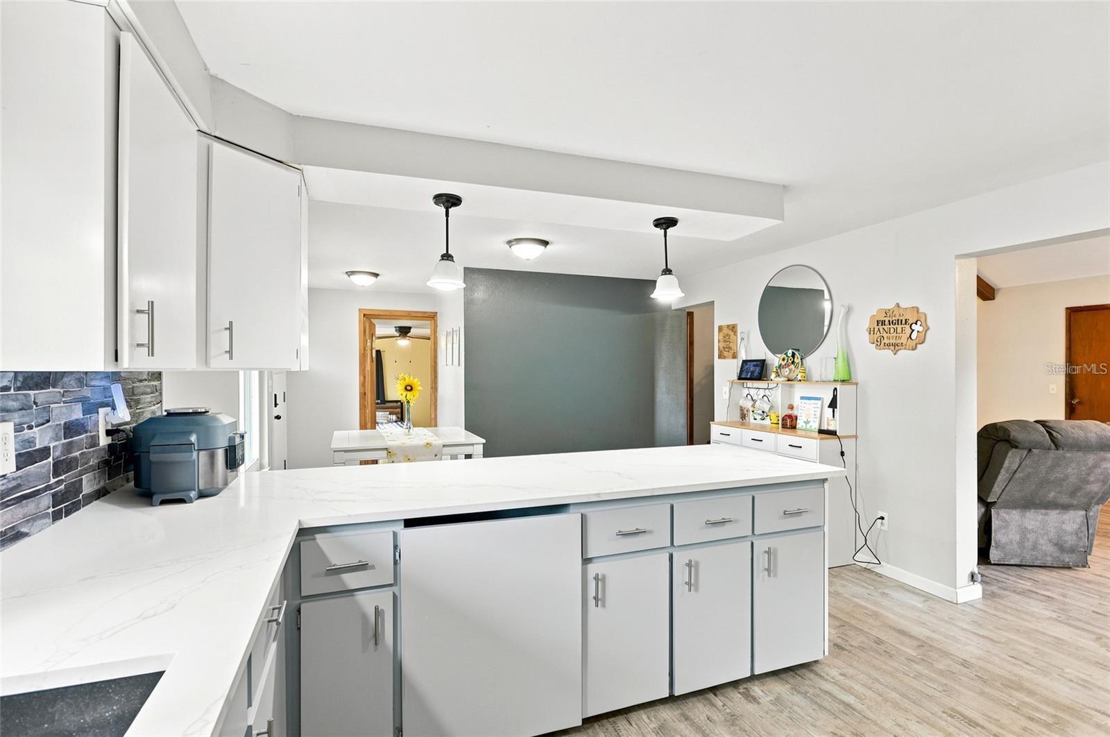 Kitchen with a large white island, gray cabinetry, pendant lights, and a dark stone backsplash.