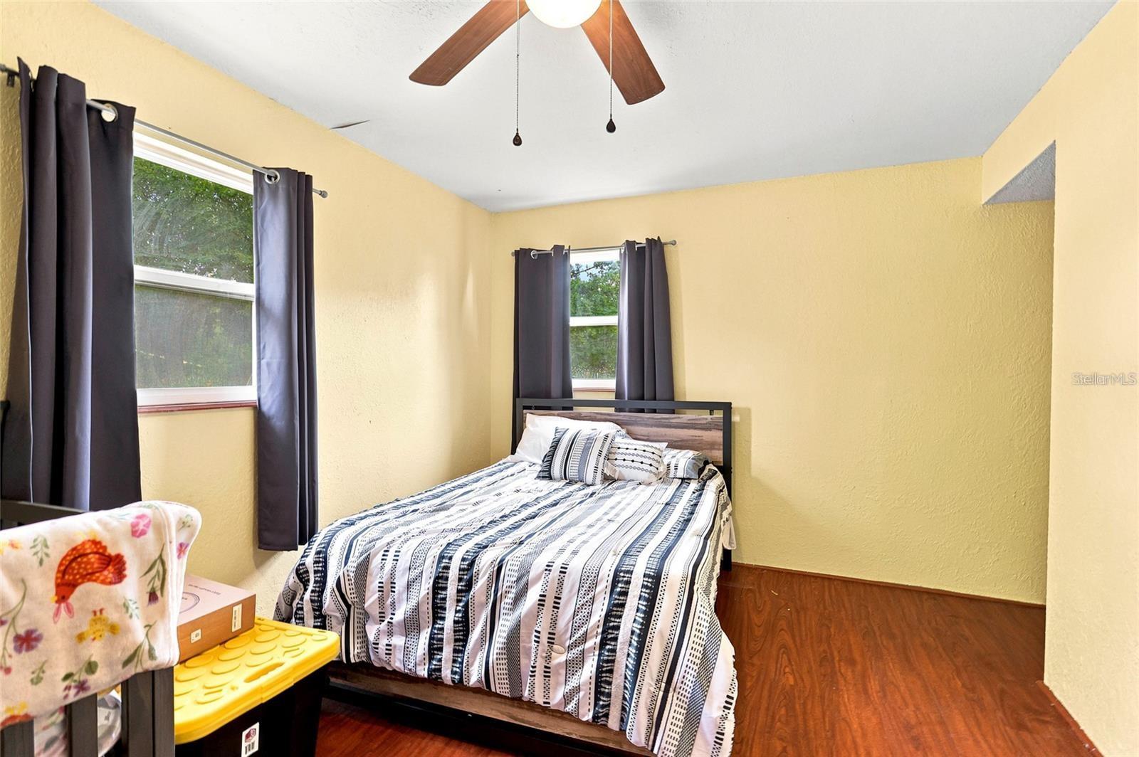 Bedroom with a black-and-white striped bedspread, yellow walls, and two curtained windows.