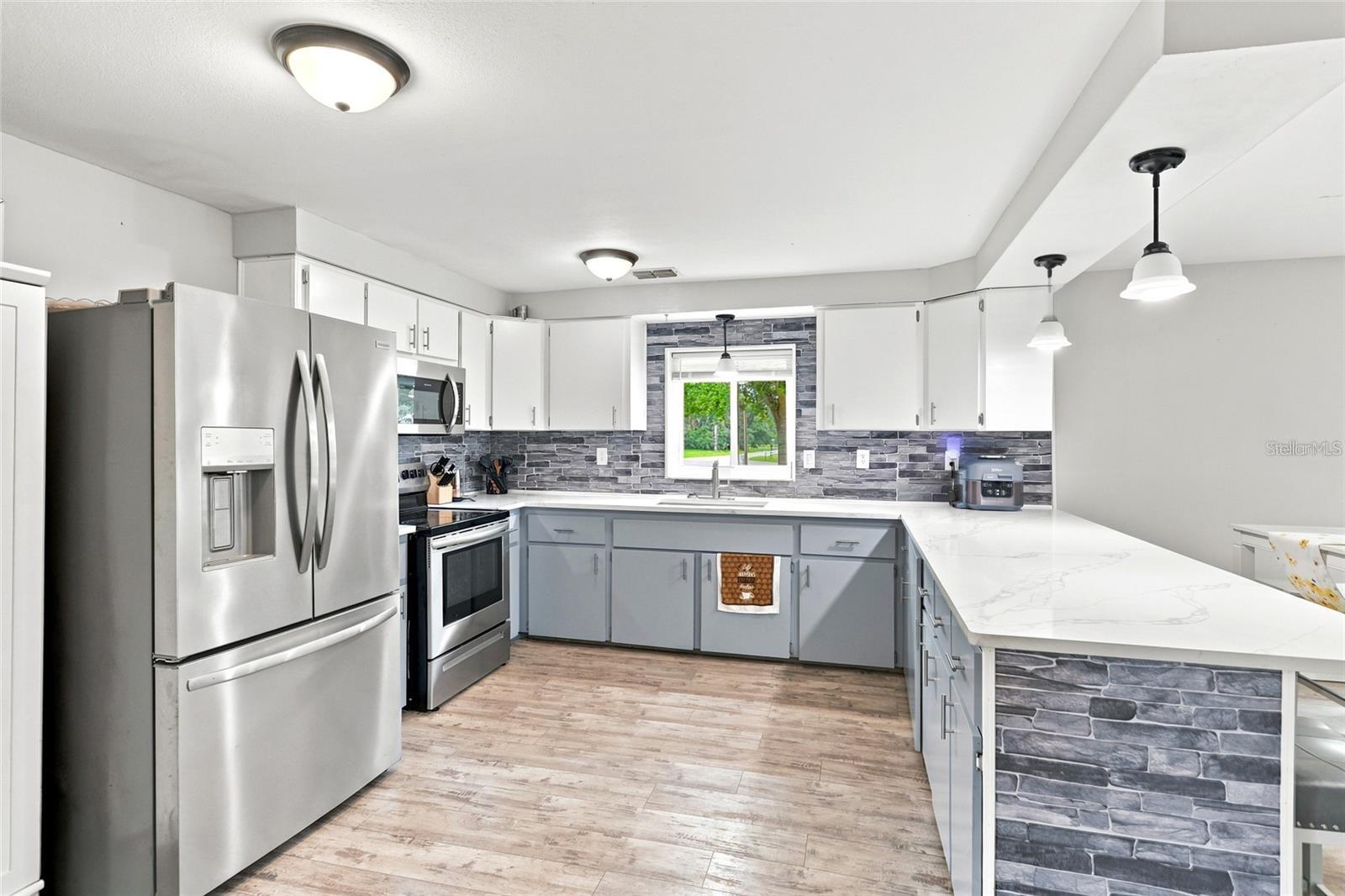 Renovated kitchen with stainless steel appliances, gray stone backsplash, and a large white peninsula.