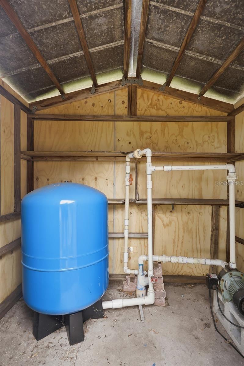 Blue pressure tank and PVC plumbing inside a plywood well-equipment enclosure.