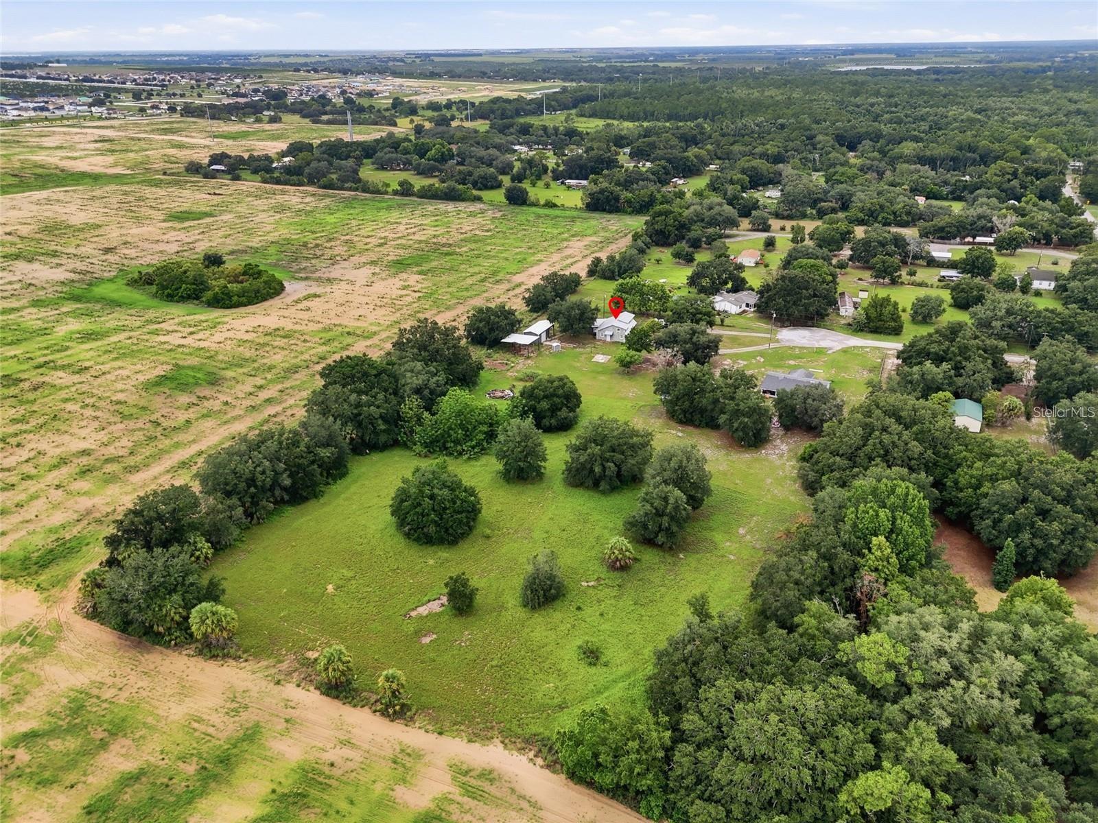 Aerial view of a rural property with a small house, open grassy land, and scattered trees.