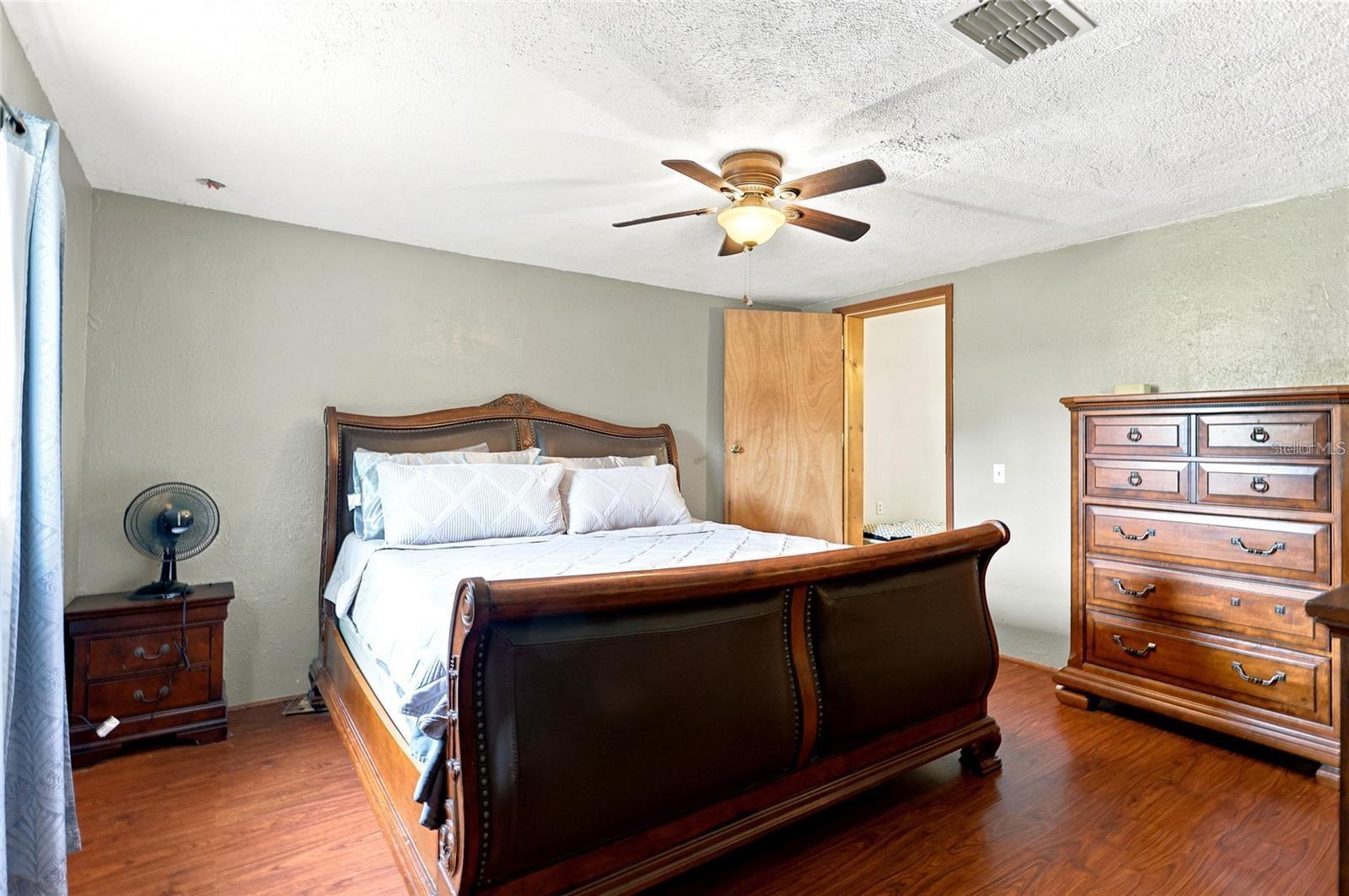 Bedroom with a dark wood sleigh bed, white bedding, matching dressers, and wood-look floors.