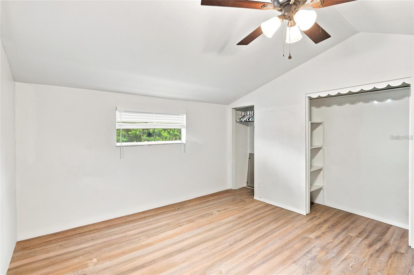 Empty bedroom with wood-look flooring, a ceiling fan, and an open closet.