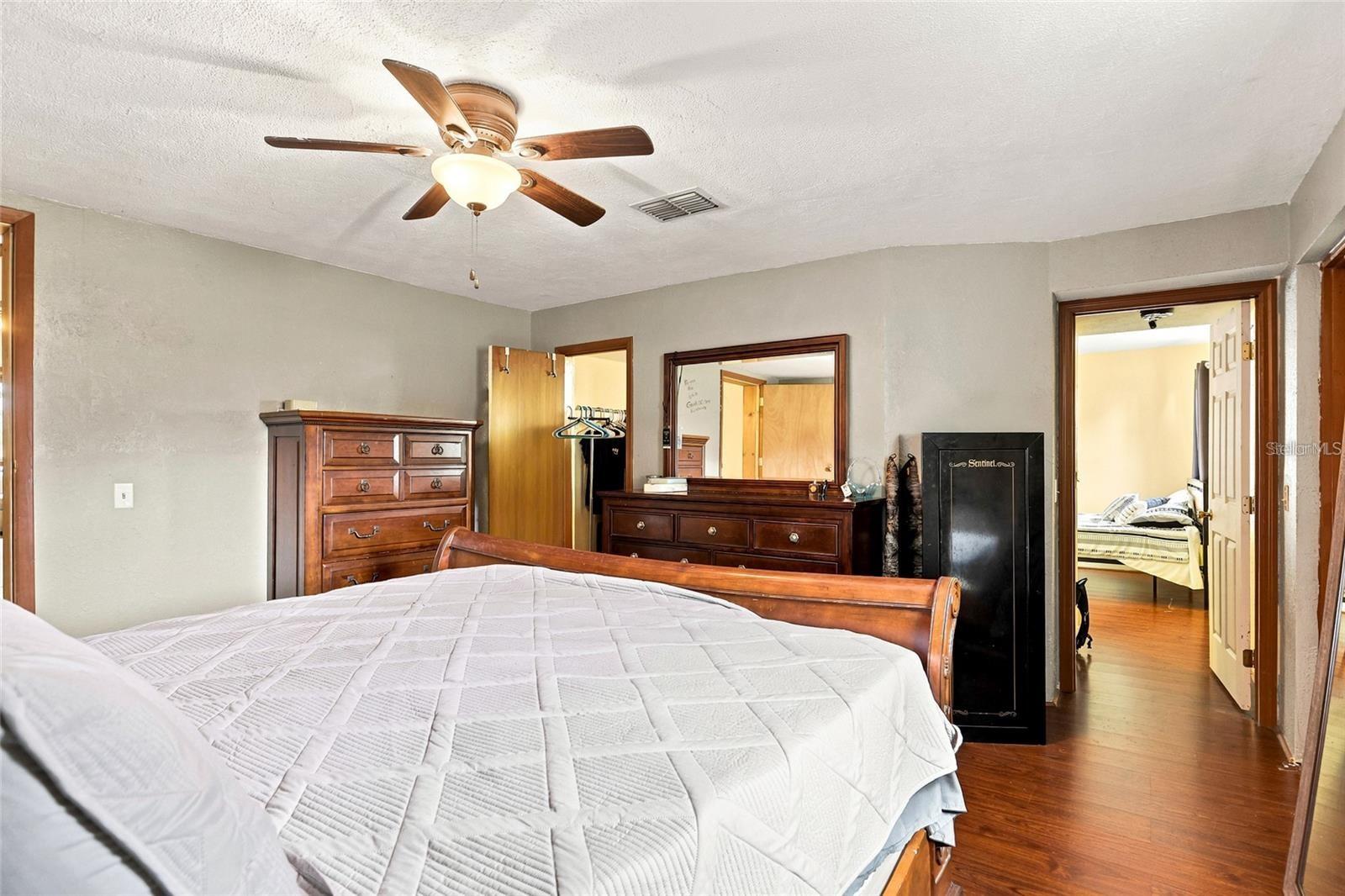 Bedroom with a white quilted bed, dark wood dressers, and a ceiling fan.