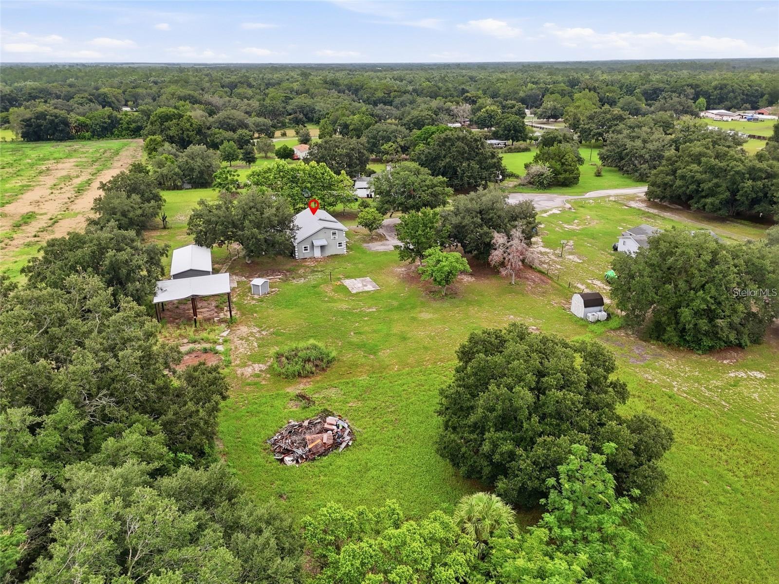 Aerial view of a gray house and outbuildings amid grassy land and mature trees.