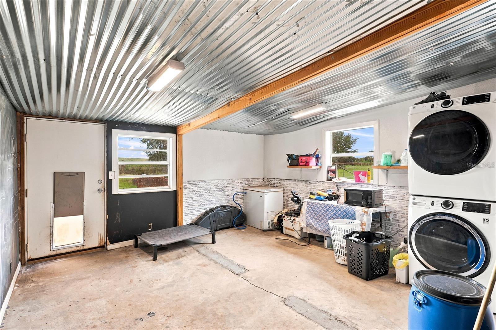 Garage laundry area with a corrugated metal ceiling, concrete floor, and stacked washer and dryer.