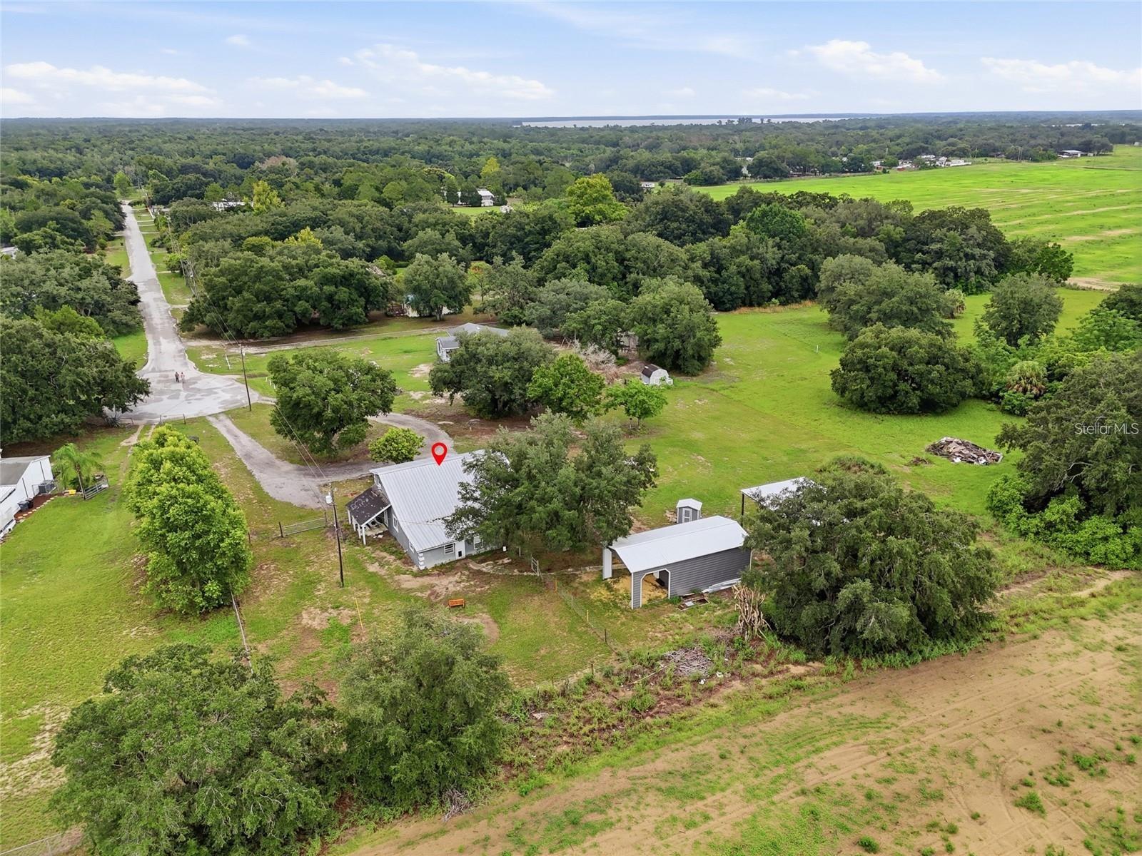 Aerial view of a gray-roofed house and outbuilding amid open grassy land and scattered trees.