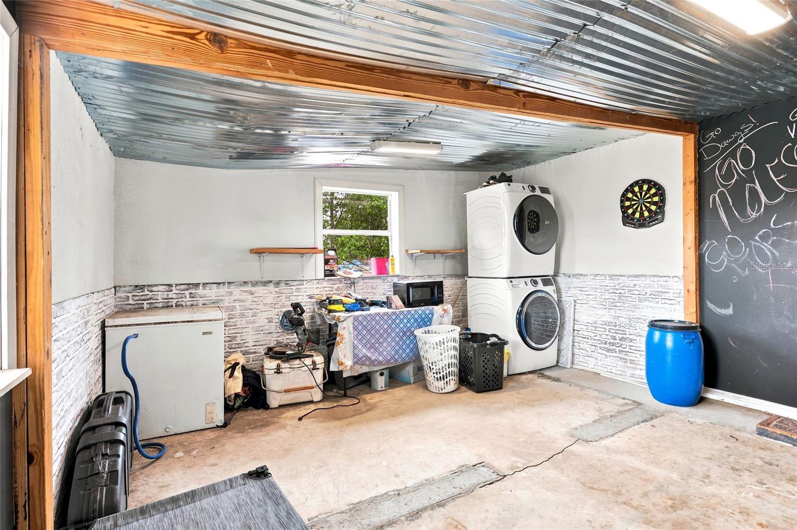 Garage laundry area with stacked washer and dryer, a chest freezer, and a dartboard.