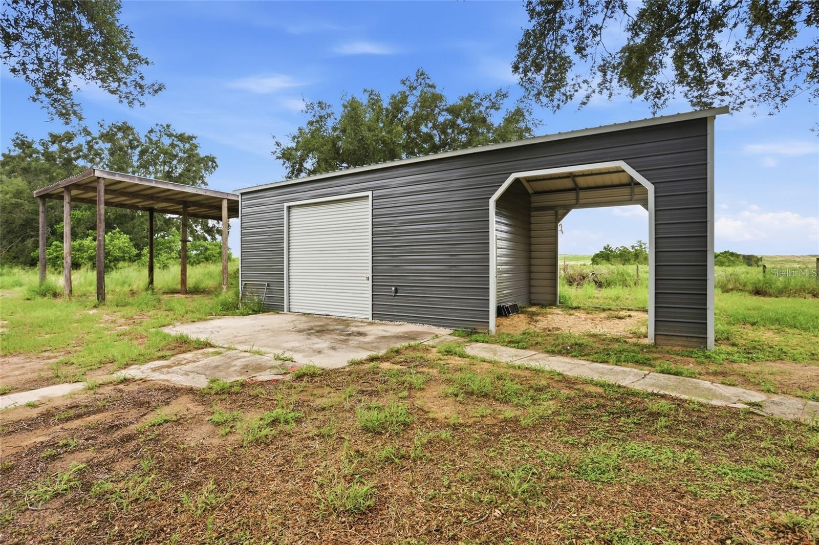 Gray metal garage with a roll-up door and open bay beside a wooden shelter.