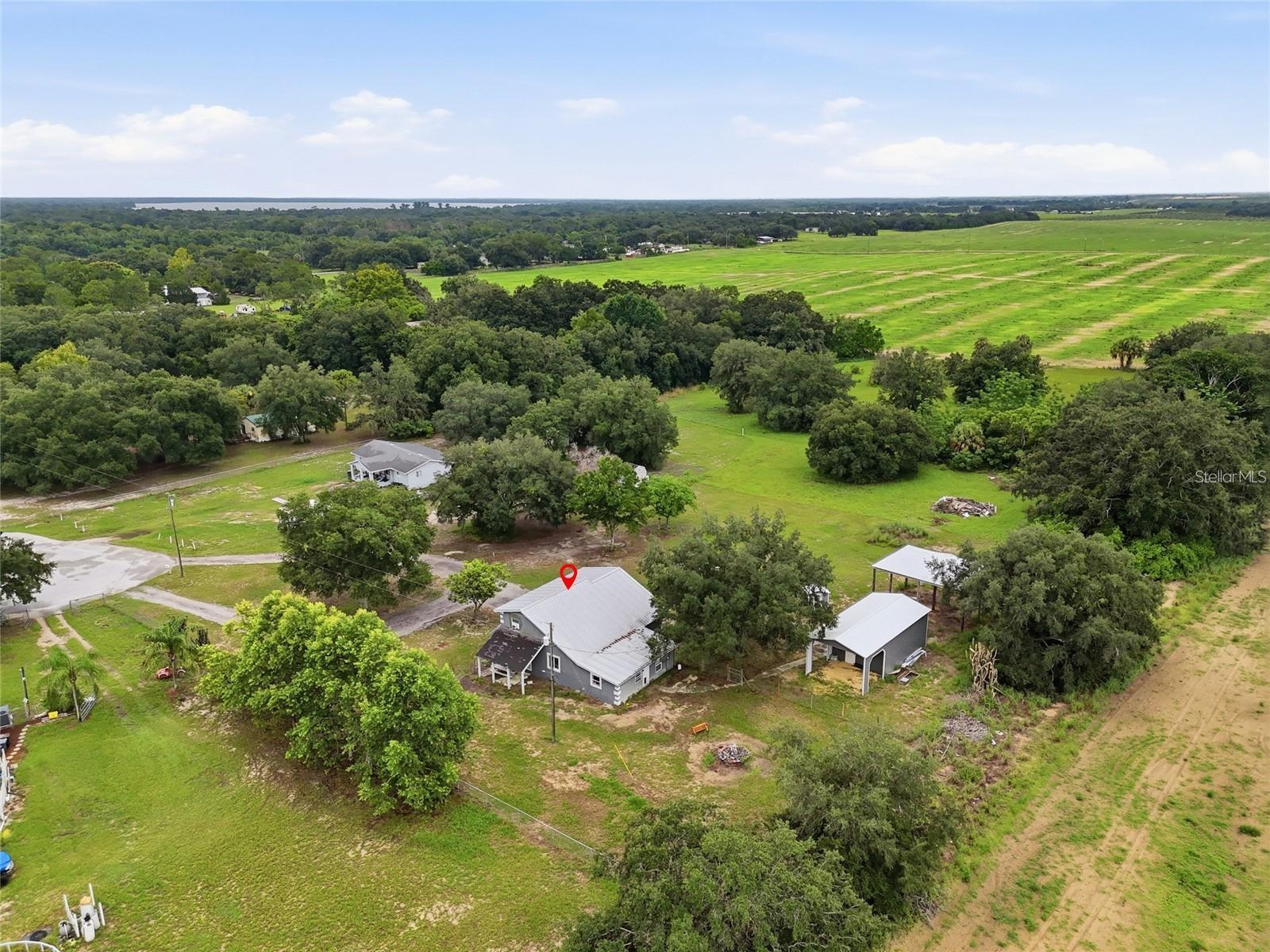 Aerial view of a gray-roofed house among trees, open land, and fields.