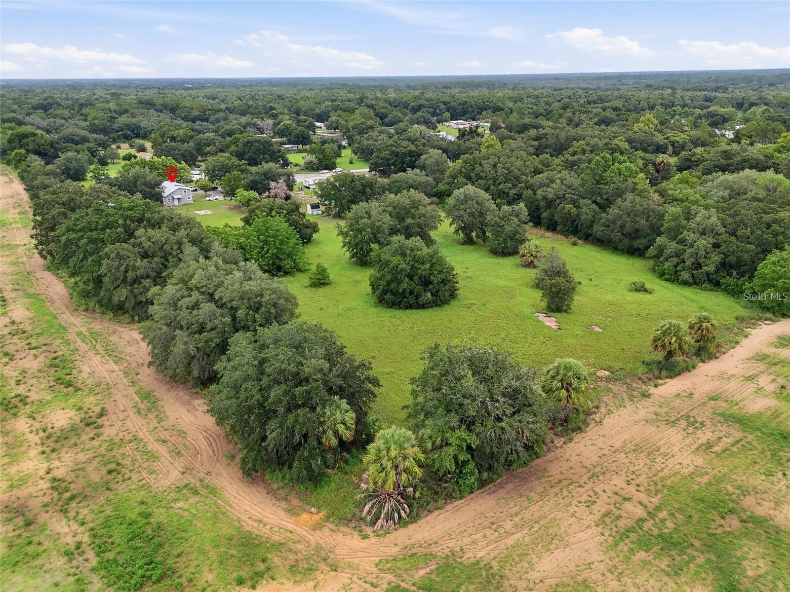 Aerial view of a home on open grassy acreage surrounded by mature trees and sandy tracks.