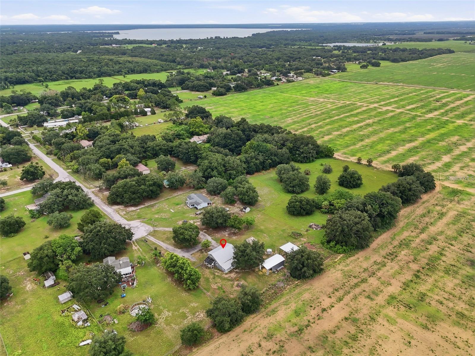 Aerial view of a rural home and surrounding fields, woods, and distant lake; red pin marks the property.