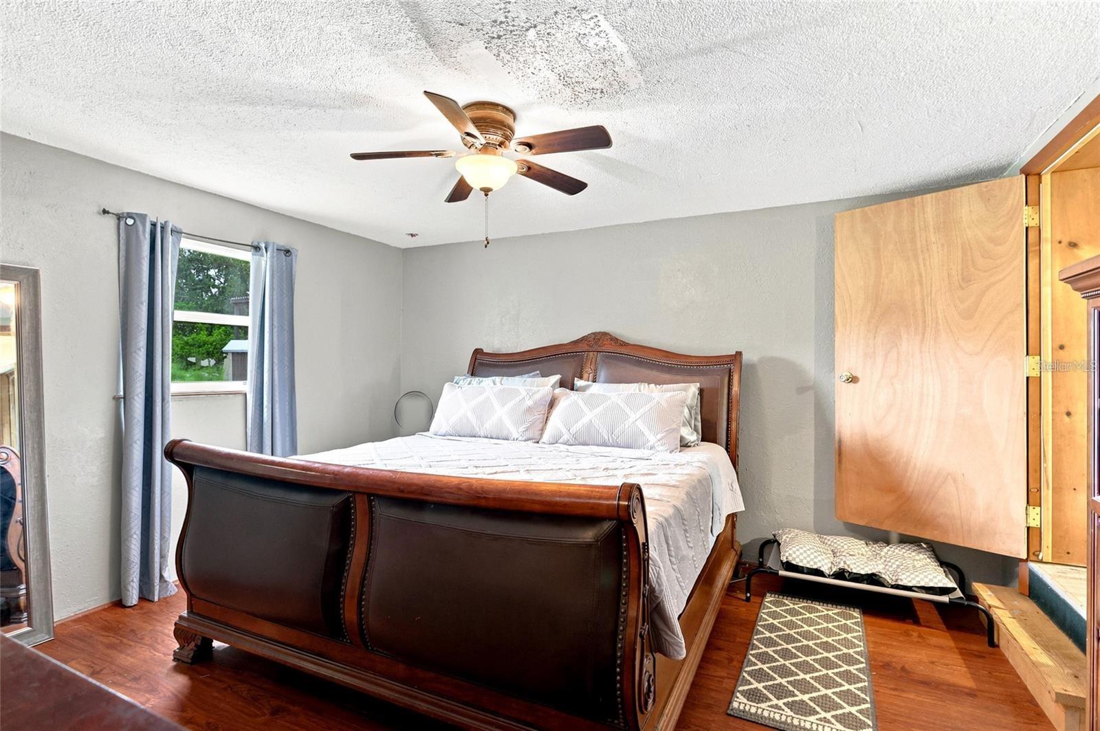 Furnished bedroom with a large dark wood bed, hardwood floors, and an open wooden closet.