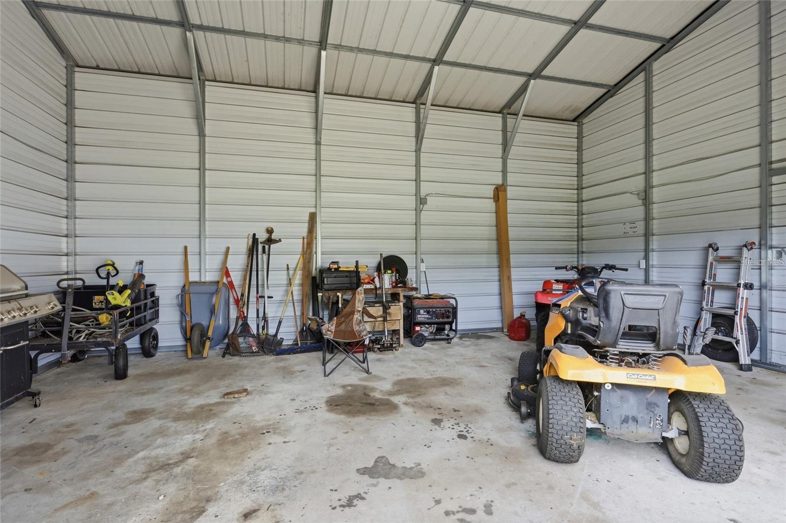 Metal garage interior with a yellow riding mower, tools, ladders, and equipment.