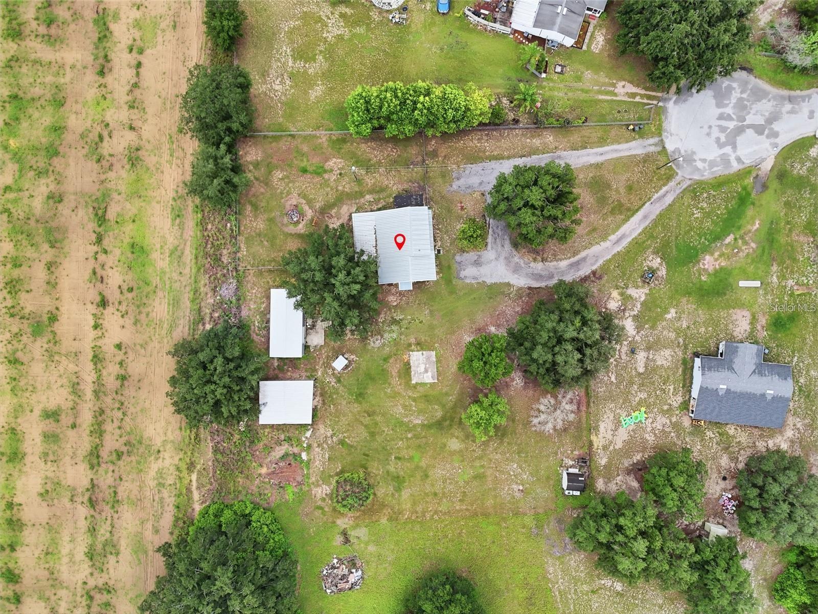 Aerial view of a light-roofed building among open land and trees, marked with a red location pin.