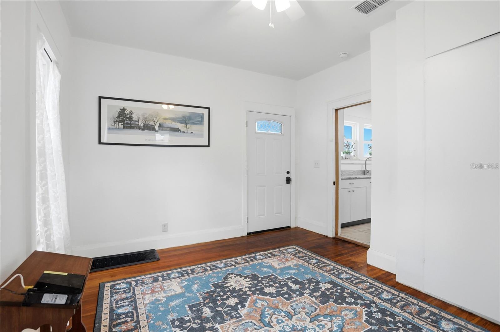 Entry room with a white front door, hardwood floors, and a large patterned rug.