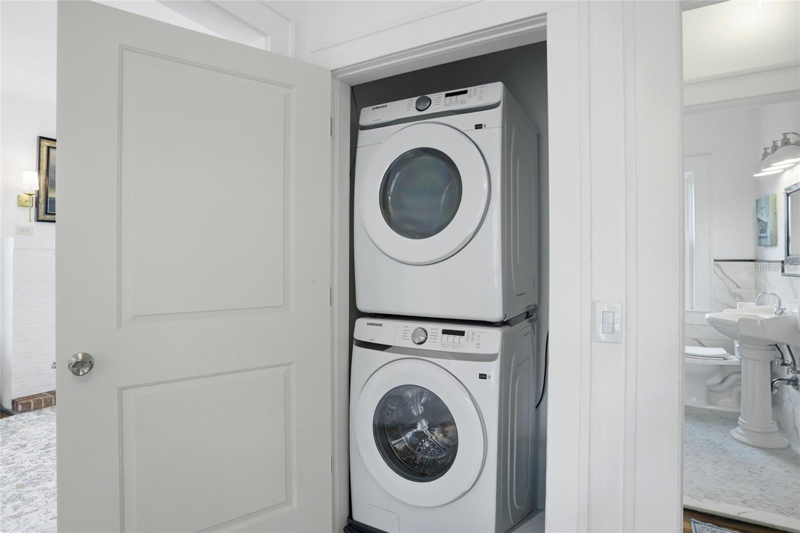 Stacked Samsung washer and dryer in a closet beside a bathroom.