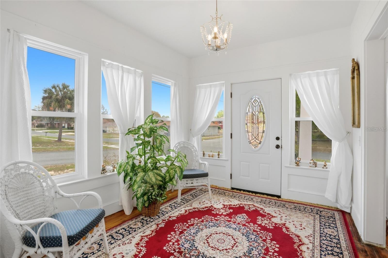 Bright entryway with a decorative glass front door, curtained windows, wicker chairs, and a red patterned rug.