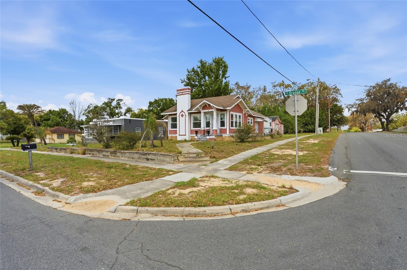 Coral-pink cottage with a white chimney and front porch on a corner lot.