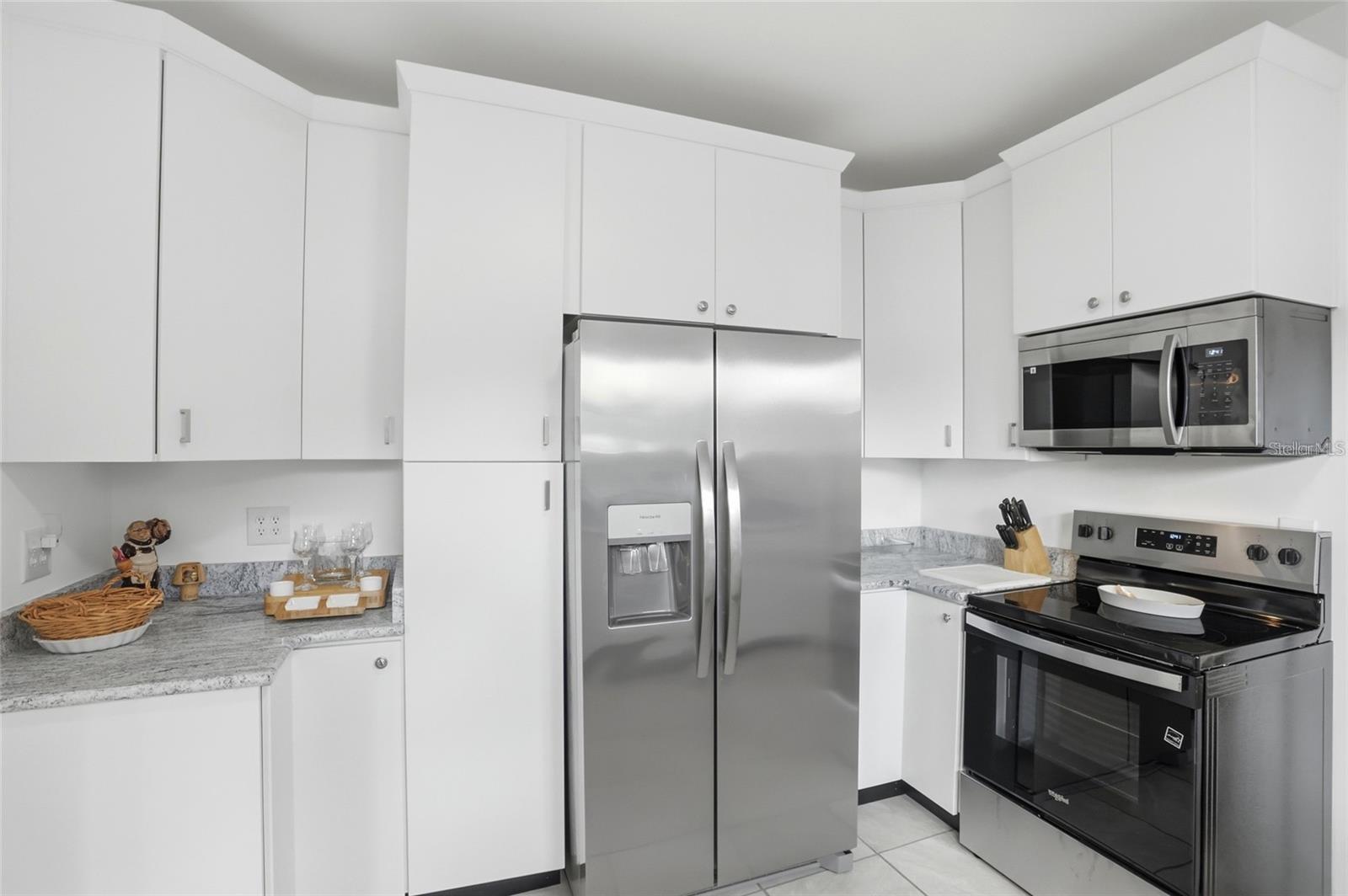 Kitchen with white cabinetry, gray marbled counters, and stainless steel appliances.