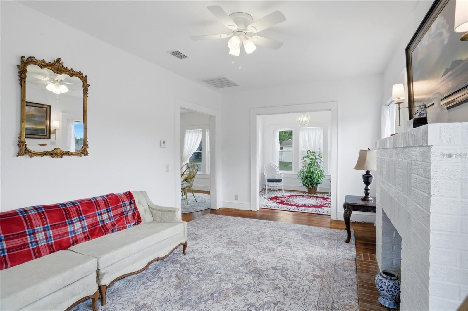 Living room with a white sofa, red plaid throw, ornate mirror, and white brick fireplace.