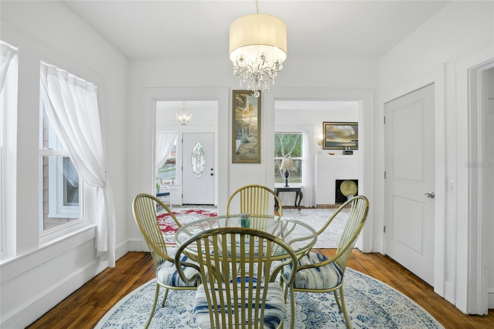 Dining room with a glass-top table, striped chairs, chandelier, and hardwood floors.