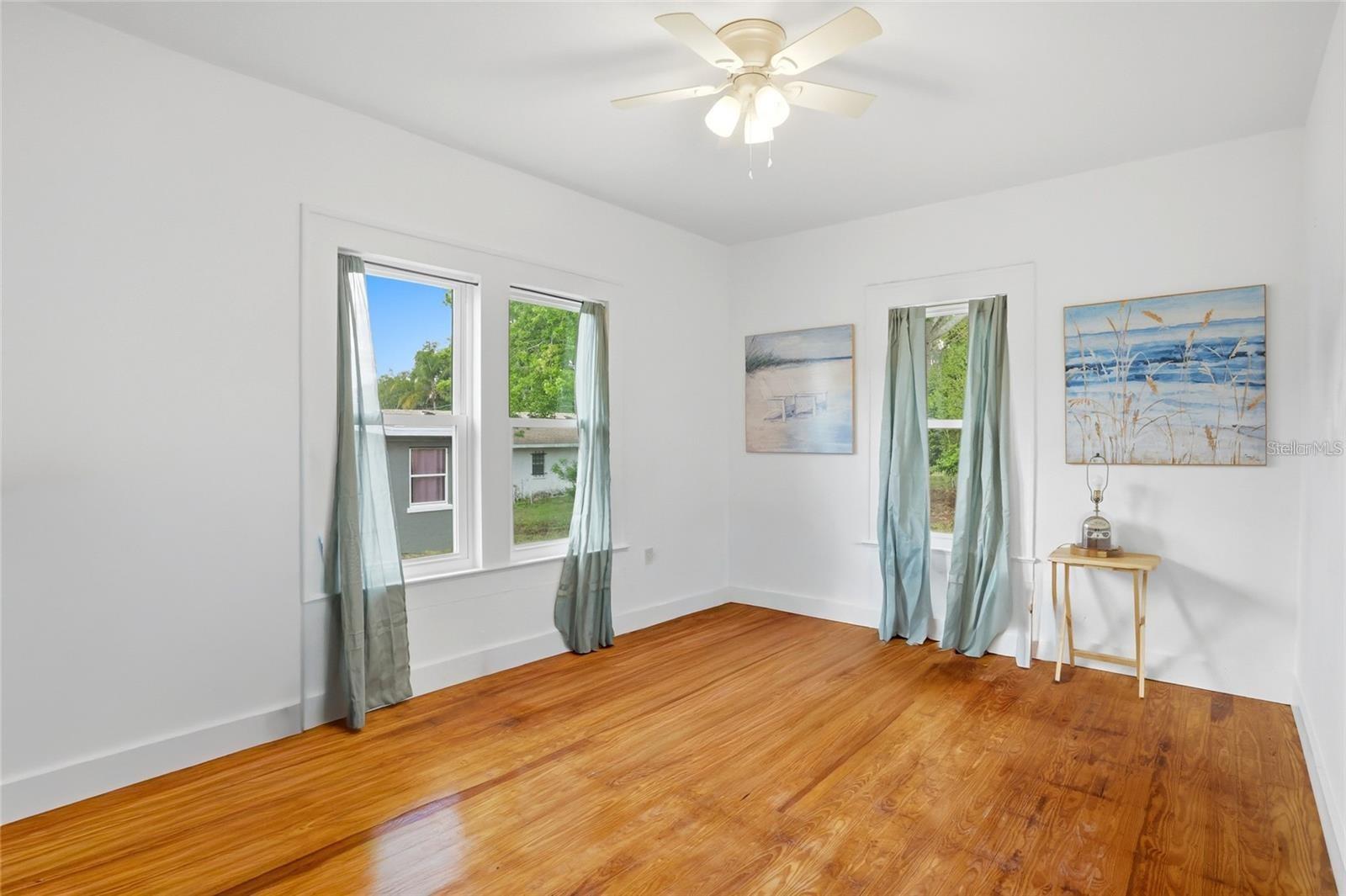Bright room with polished hardwood floors, curtained windows, and a ceiling fan.