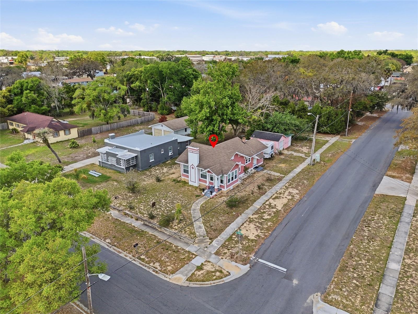 Aerial view of a pink-and-white house on a corner lot, marked with a red location pin.