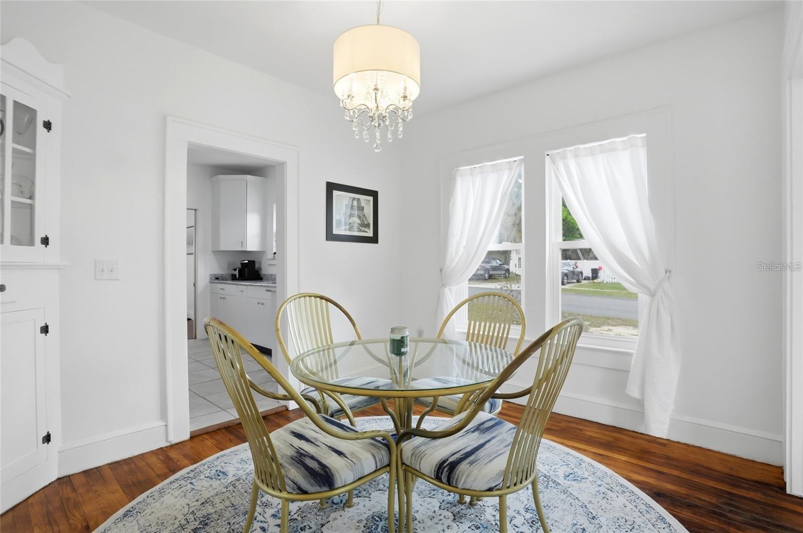 Dining room with a glass-top table, gold-toned chairs, chandelier, and curtained windows.