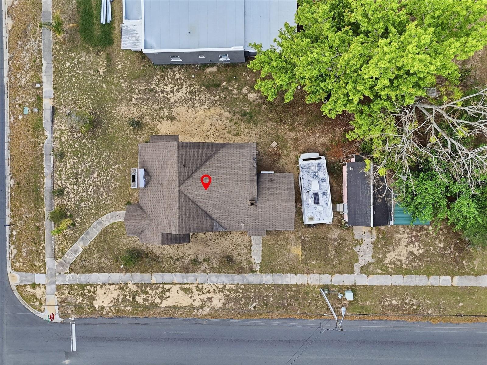 Aerial view of a home and its yard, with mature trees and neighboring buildings.