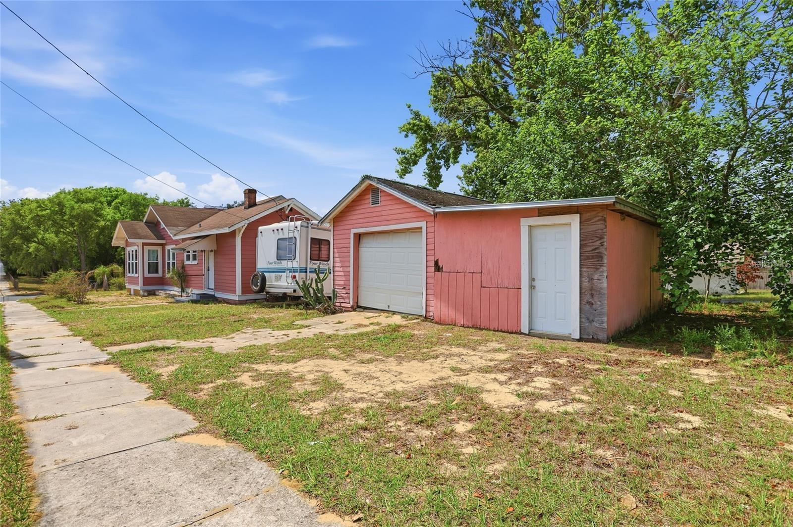 Pink house and detached garage with a camper parked between them, viewed from the sidewalk.
