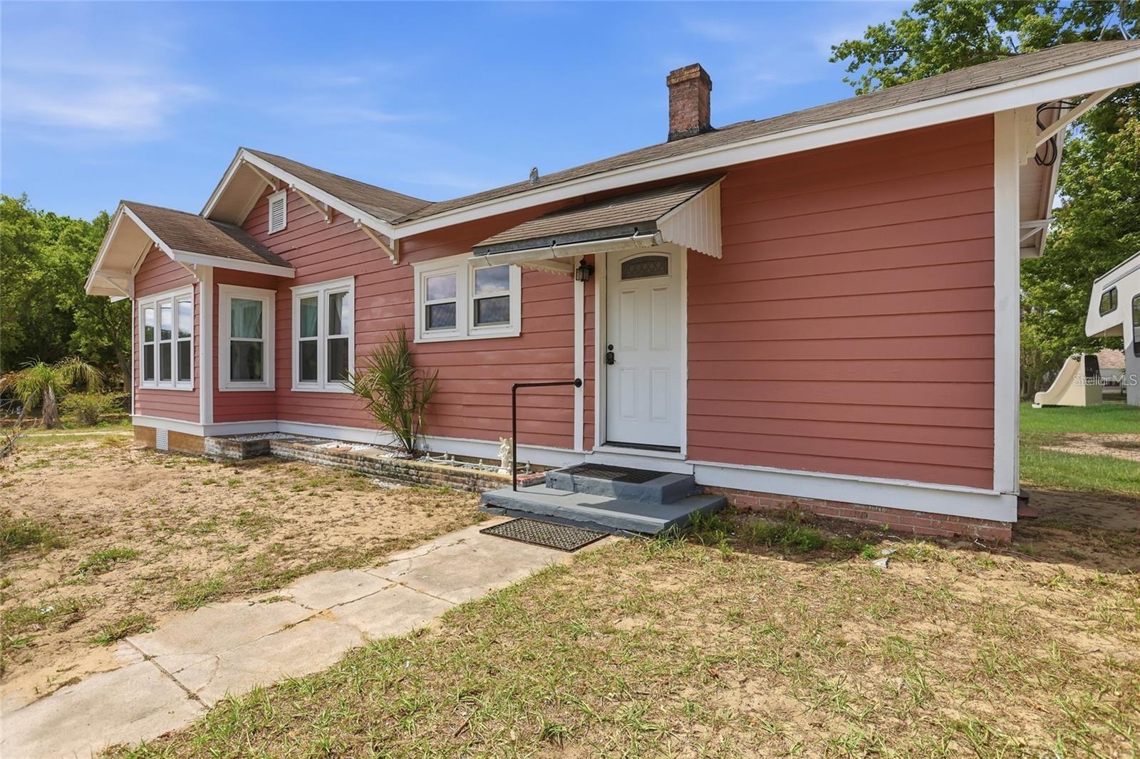 Coral-pink single-story house with white trim, a front awning, and a concrete walkway.