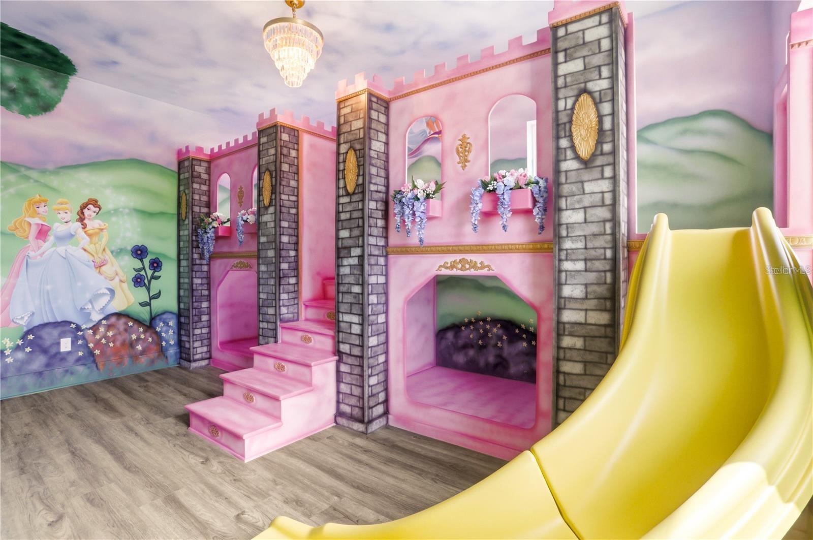 Children’s playroom with a pink castle structure, princess mural, and large yellow slide.