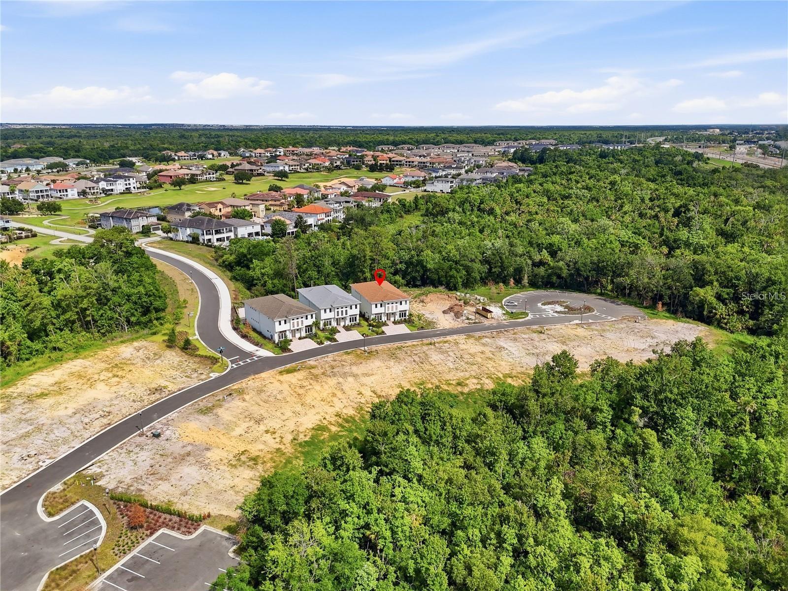 Aerial view of a marked home in a new neighborhood bordered by wooded land and undeveloped lots.