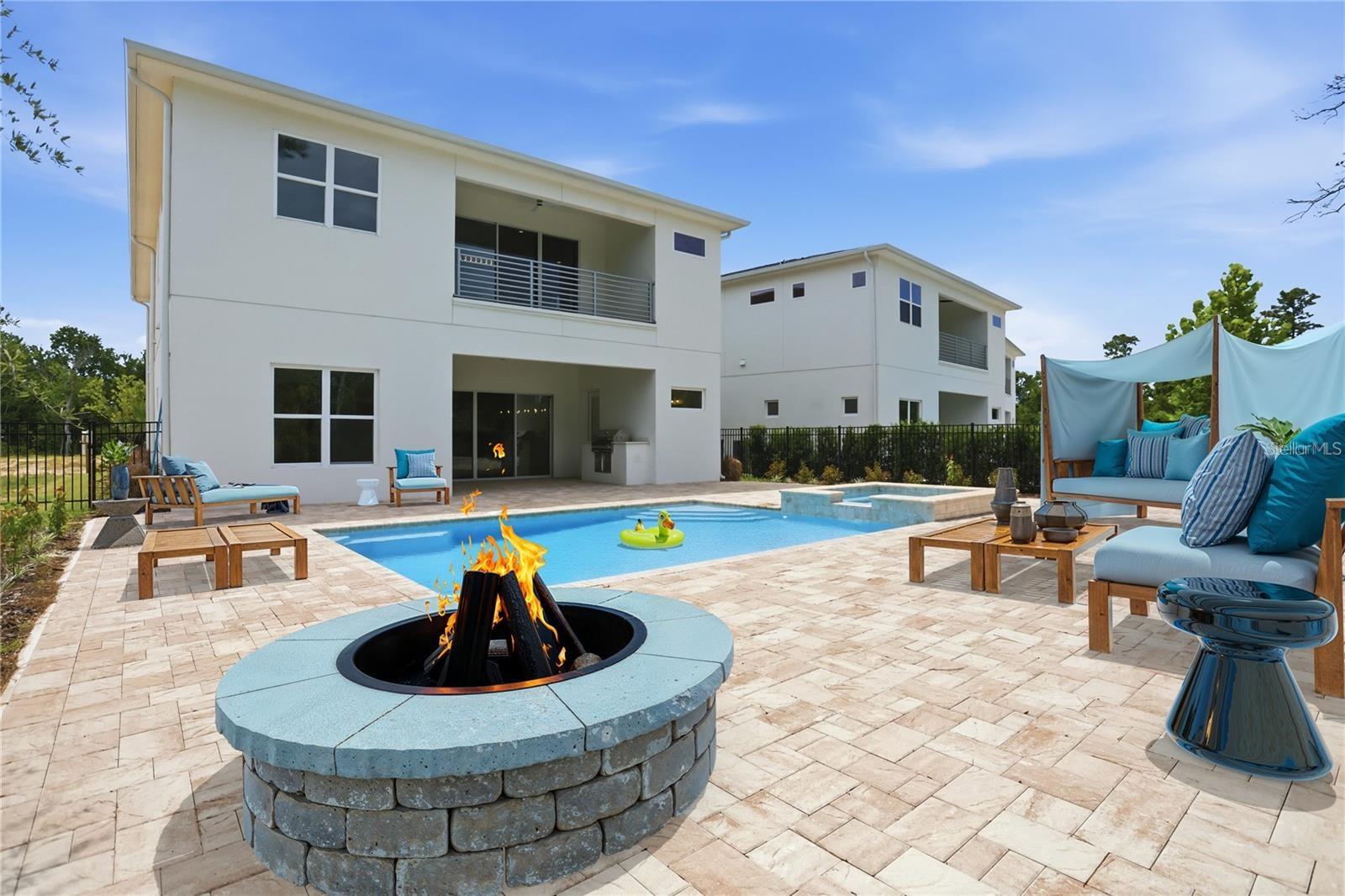Modern two-story home behind a pool and patio with a circular fire pit and lounge seating.
