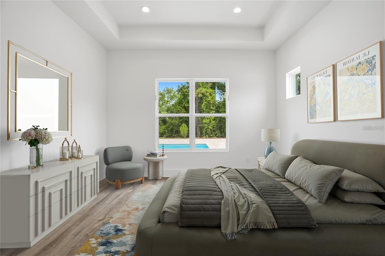 Staged bedroom with a large gray bed and a window overlooking a pool.