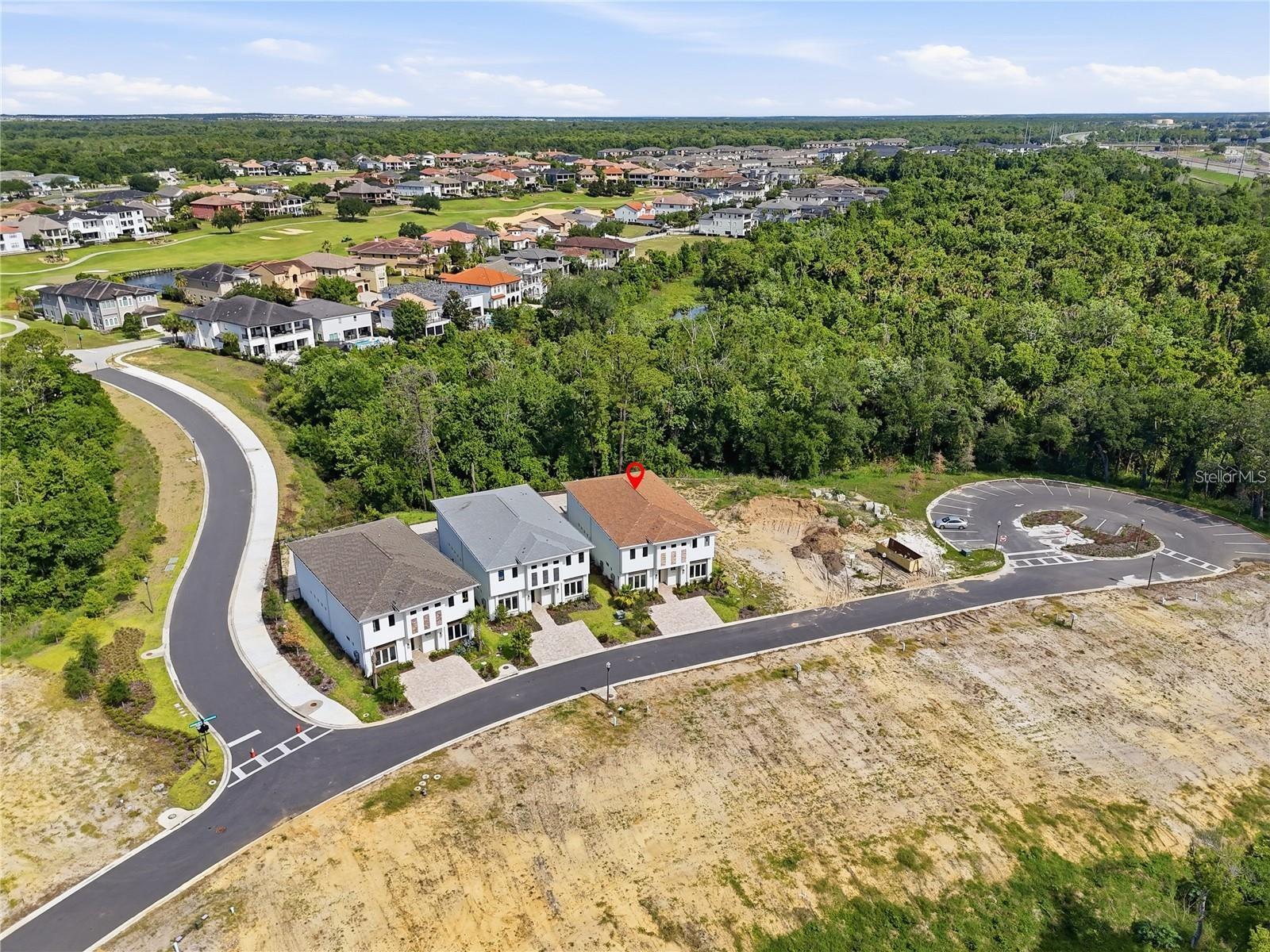 Aerial view of a marked two-story home beside a wooded area, with nearby homes and a golf course.