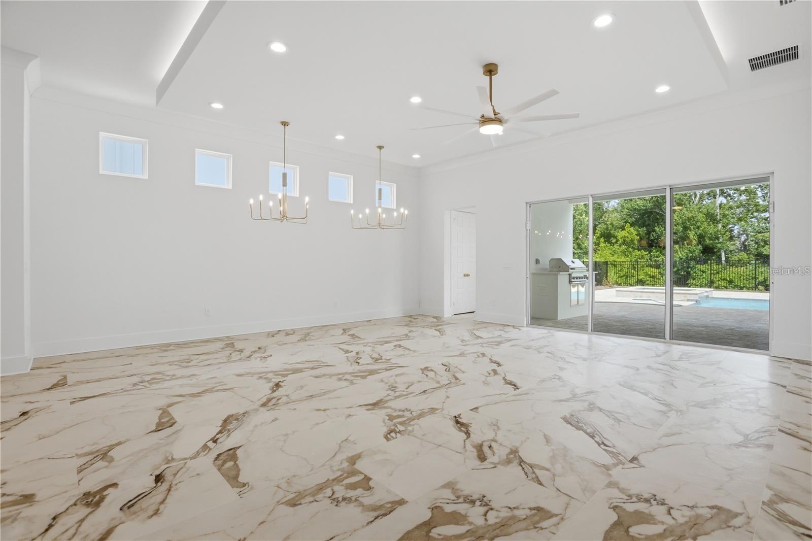 Vacant living area with marble-look floors, two chandeliers, and sliding doors overlooking a pool.