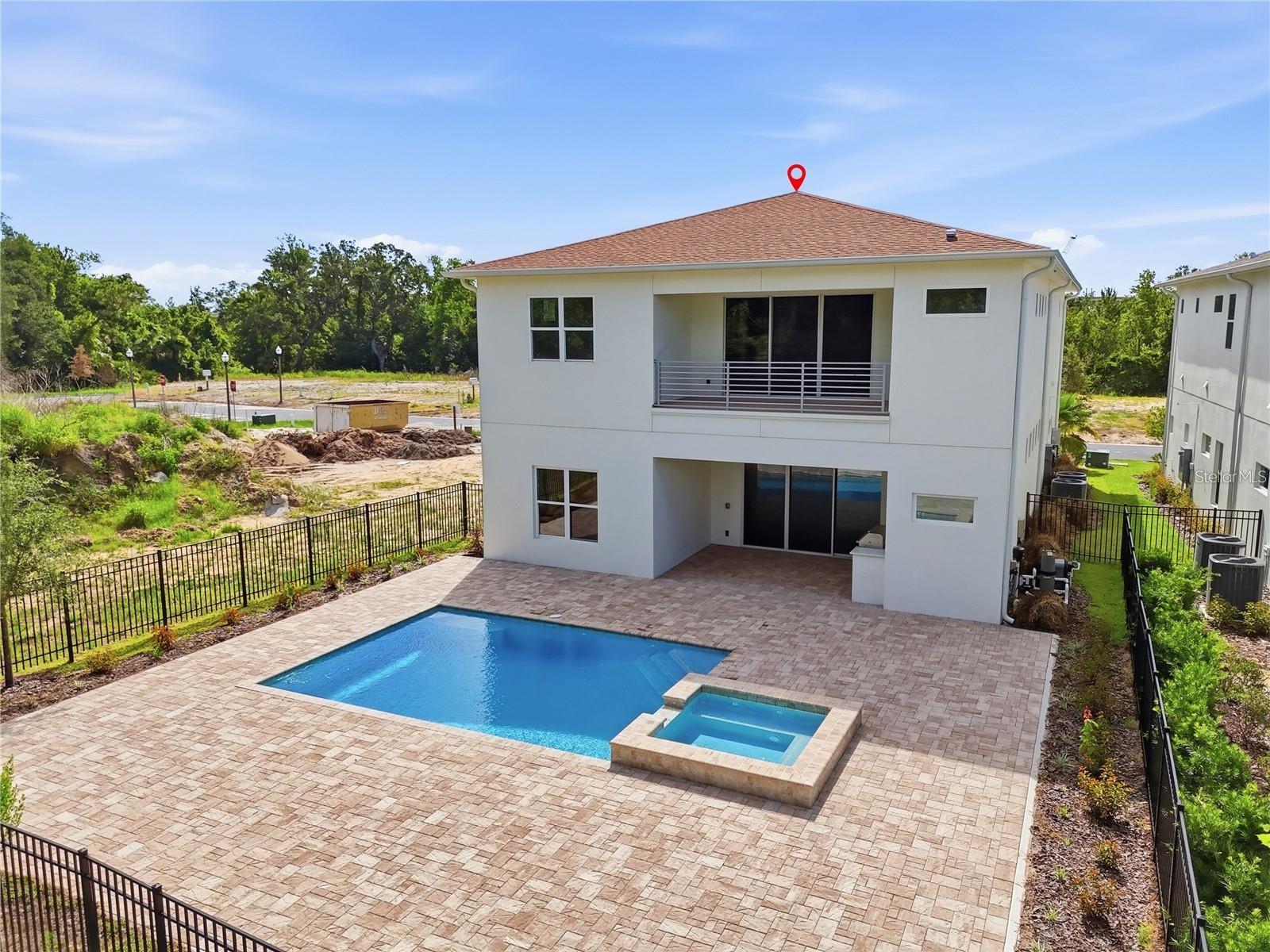 Rear of a two-story white home with a balcony, fenced patio, swimming pool, and attached spa.