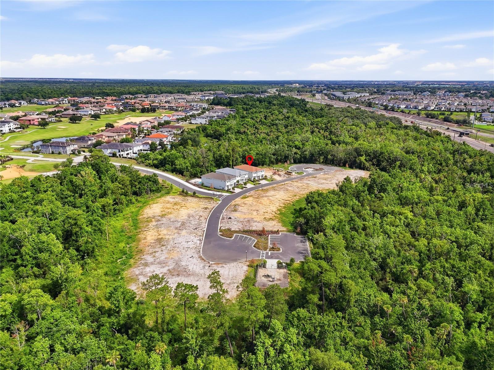 Aerial view of 7626 Whitemarsh Way beside dense woodland, cleared land, and nearby homes.