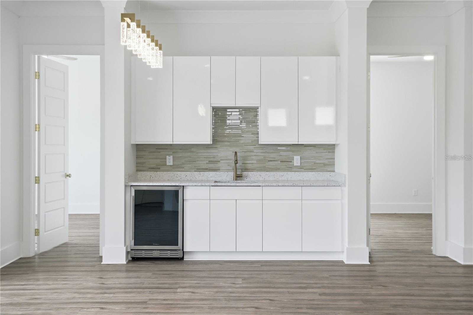 Modern kitchen with glossy white cabinets, gray tile backsplash, beverage refrigerator, and geometric pendant light.
