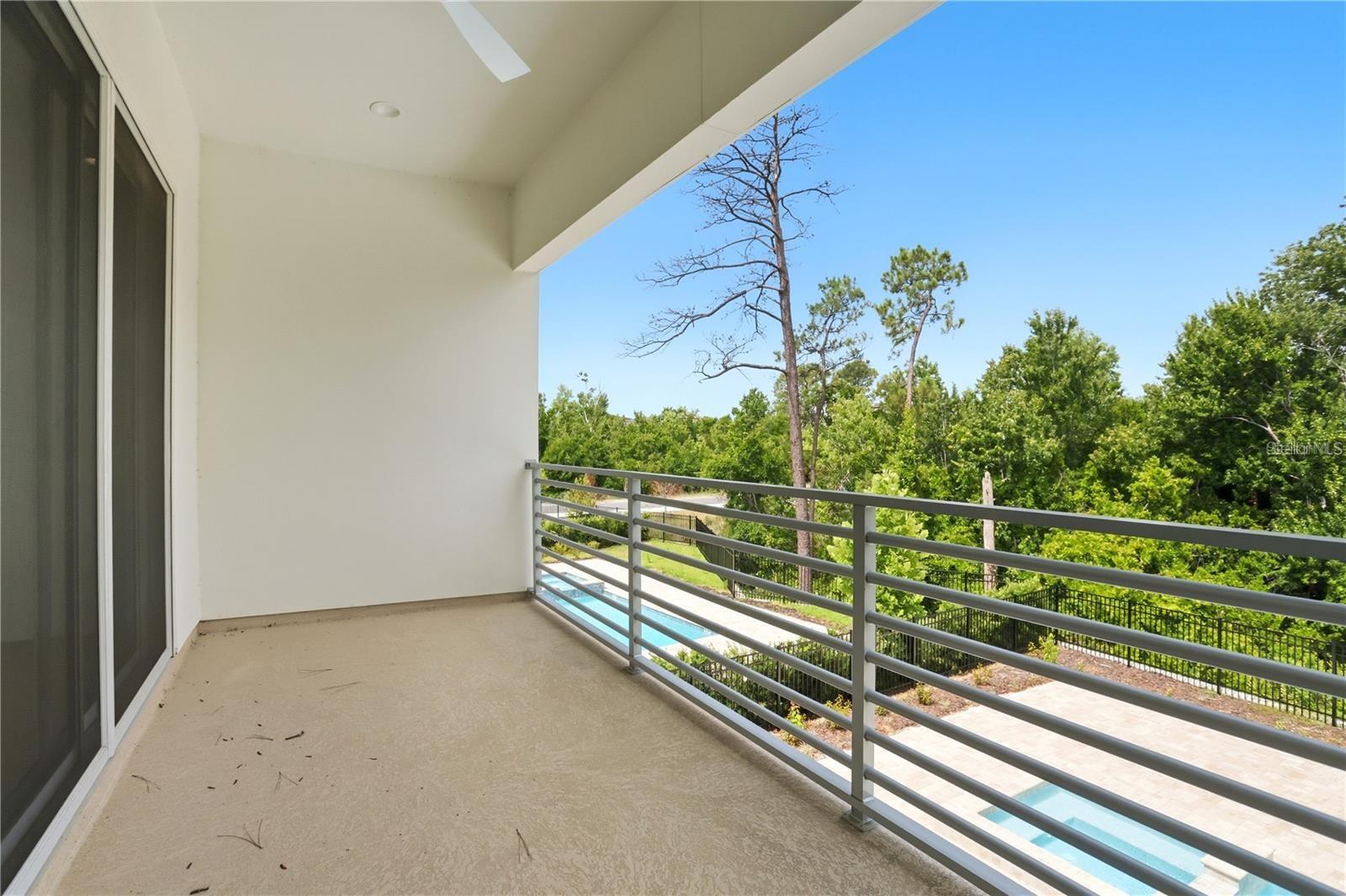 Covered balcony overlooking a swimming pool and trees, with a gray metal railing.