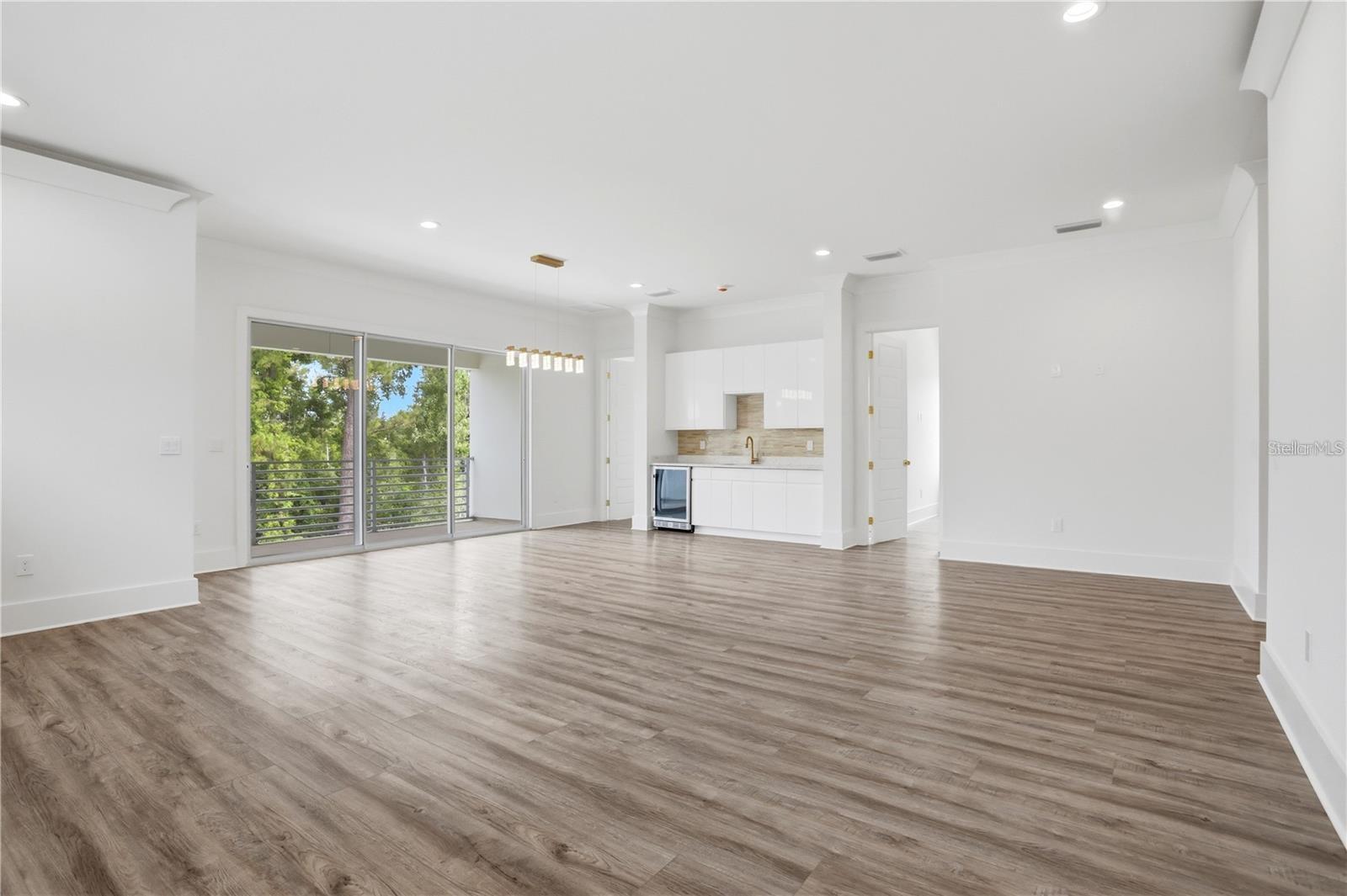 Vacant living area with plank flooring, sliding glass doors, and a compact white kitchen.