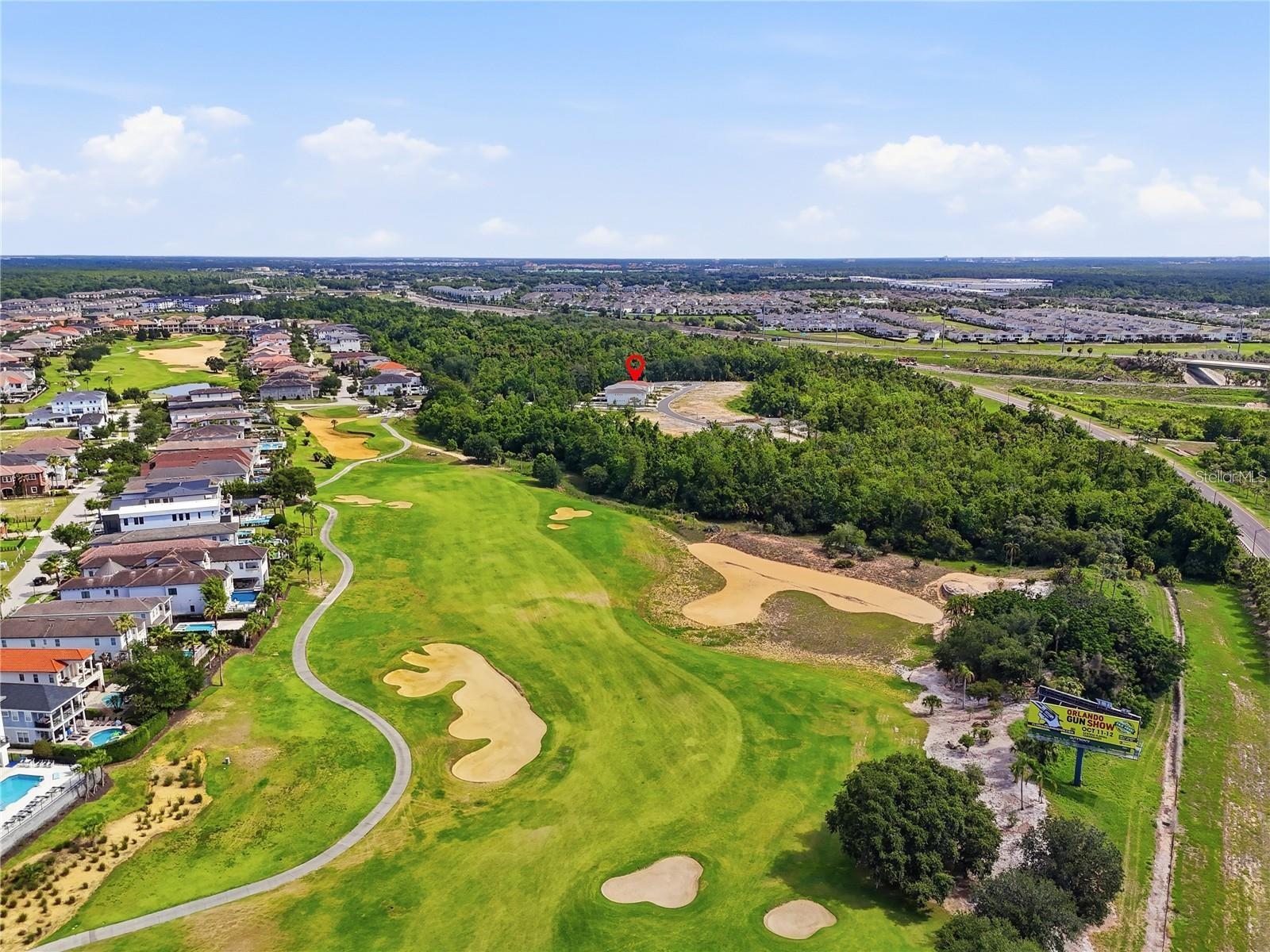 Aerial view of a golf course and surrounding homes, with a red pin marking a property.