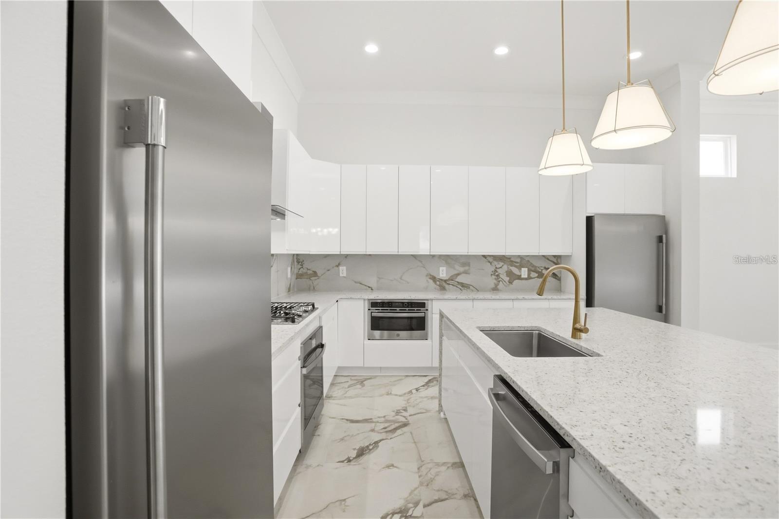 Modern white kitchen with stainless steel appliances, marble-pattern surfaces, and a large island.